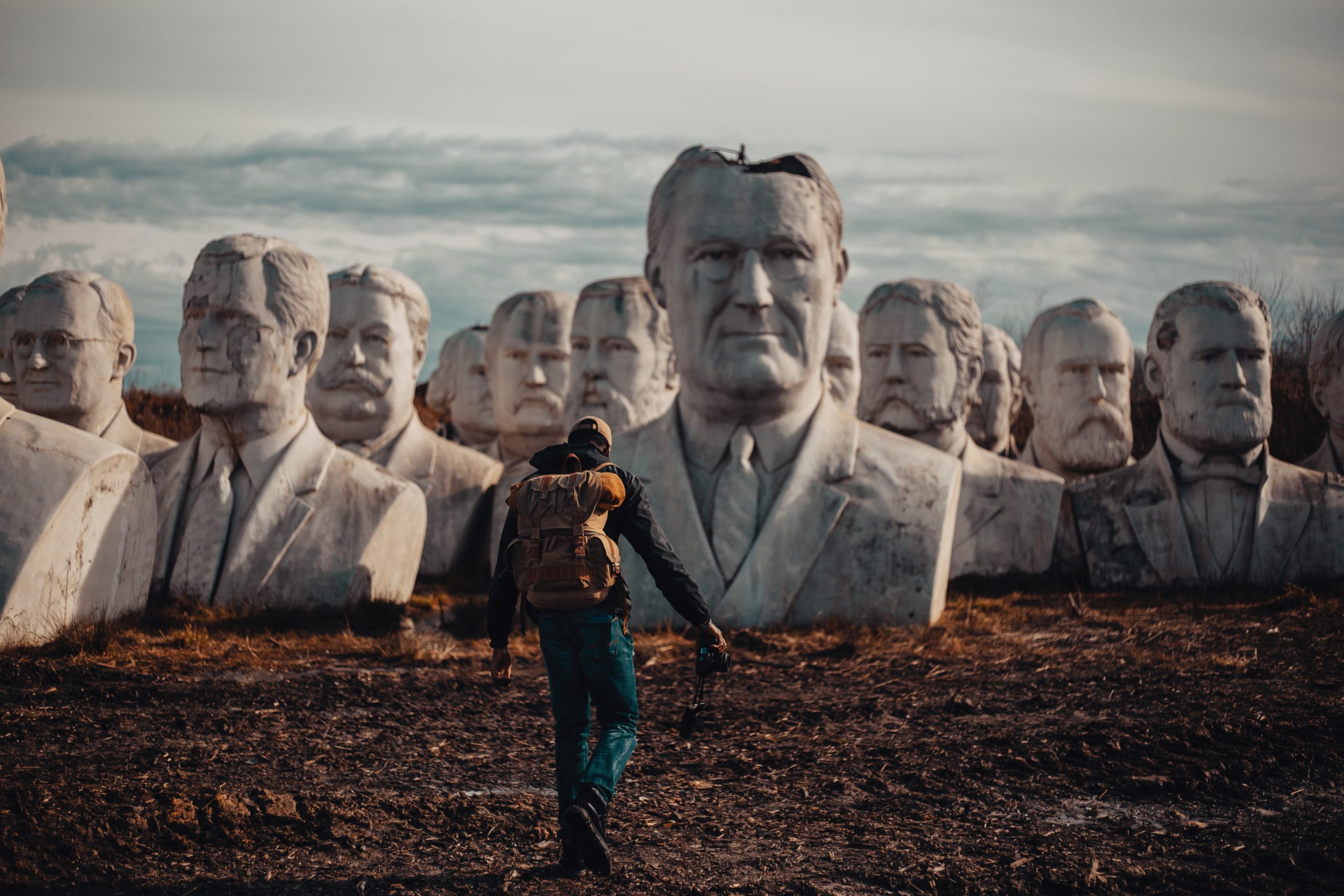 a men with a bag un his shoulders walking on field with busts of statues