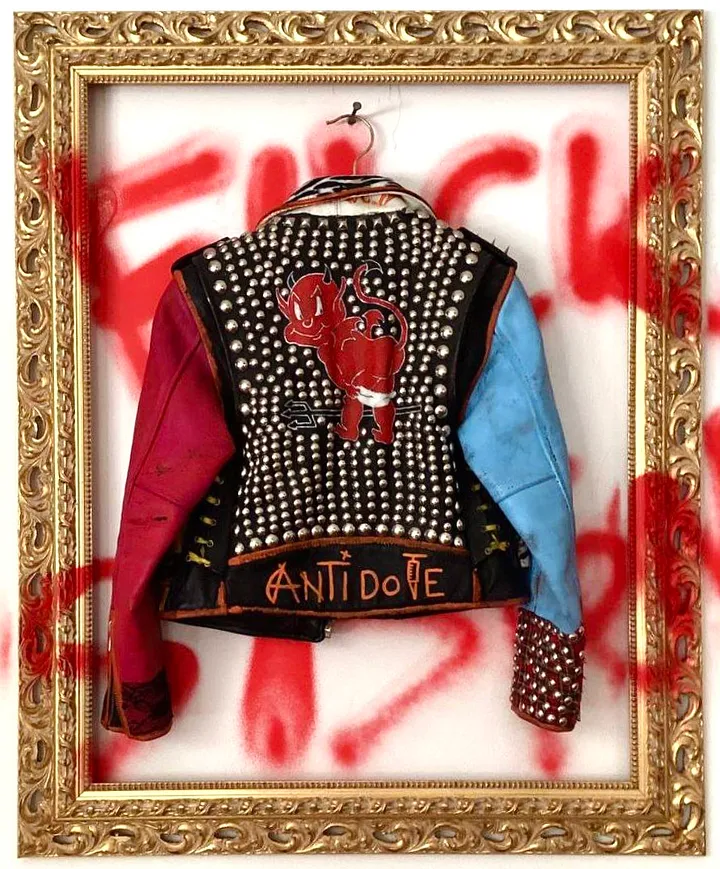 Punk style jacket with metal rivets. One sleeve of jacket in red another in blue. On the bottom title "Antidote". On the back application with smyley red cartoon devil with lowered underpants and showed his shiny naked ass.